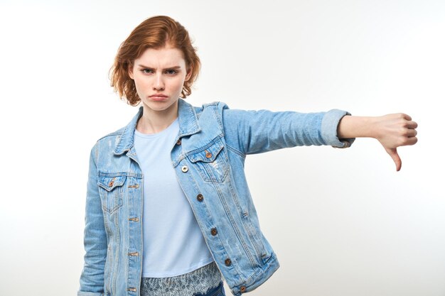 Photo portrait de jeune femme rousse mécontente montrant les pouces vers le bas isolé sur fond blanc de studio n'approuve pas quelque chose met un dislikexa