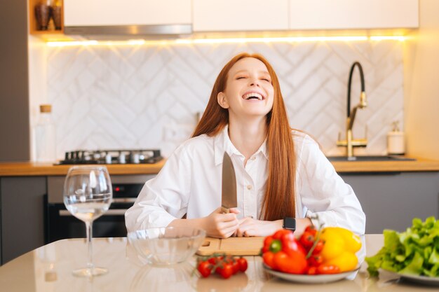 Portrait d'une jeune femme rousse séduisante aux yeux fous tenant un grand couteau assis à table avec