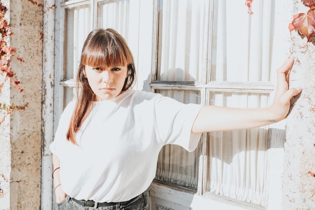 Portrait d'une jeune femme rousse sur une vieille fenêtre blanche sur attitude cool, femme sérieuse et confiante, l'avenir est femme. Chemise blanche et port moderne avec espace de copie, concept de réseau social.