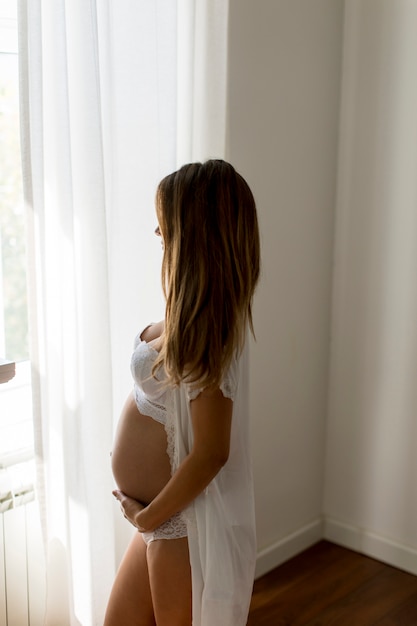 Portrait de jeune femme séduisante enceinte, debout près de la fenêtre