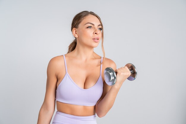 Portrait d'une jeune femme séduisante en forme de sport rose faisant des exercices avec des haltères en métal lourd