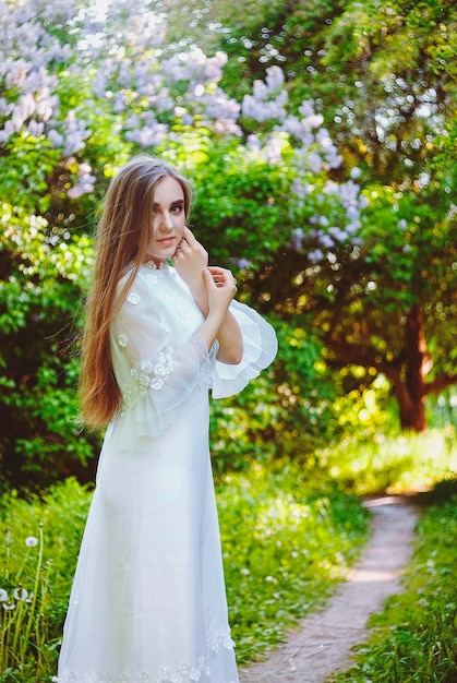Portrait de jeune femme séduisante en longue robe de mariée blanche dans le jardin de printemps avec des arbres en fleurs.
