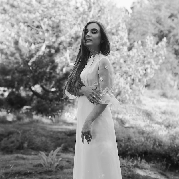 Portrait De Jeune Femme Séduisante En Longue Robe De Mariée Blanche Dans Le Jardin De Printemps Avec Des Arbres En Fleurs.