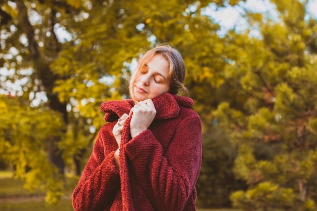 Portrait d'une jeune femme séduisante portant un élégant manteau en tissu doux, s'enveloppant, sentant la douceur du tissu. Belle fille en manteau chaud à l'ancienne debout dans le parc d'automne