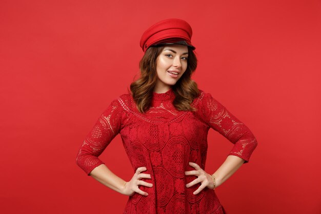 Portrait d'une jeune femme séduisante en robe de dentelle, casquette regardant la caméra debout avec les bras sur les hanches isolés sur fond de mur rouge en studio. Concept de mode de vie des émotions sincères des gens. Maquette de l'espace de copie.