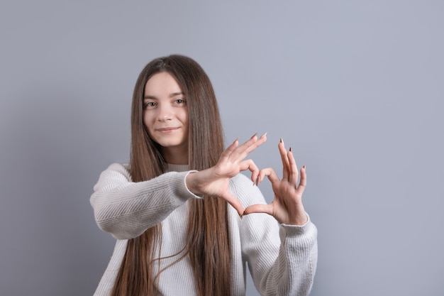 Portrait d'une jeune femme séduisante souriante montrant le geste du cœur avec deux mains et regardant la caméra isolée sur fond gris