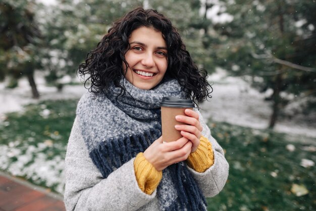 Portrait d'une jeune femme séduisante tenant un café dans un parc d'hiver enneigé.