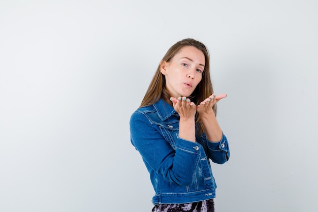 Portrait de jeune femme soufflant un baiser d'air avec des lèvres boudées en veste en jean et à la vue de face paisible