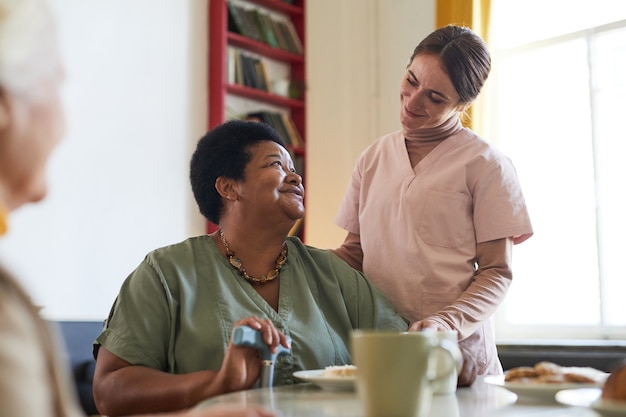 Photo portrait d'une jeune femme souriante aidant une patiente pendant le dîner à l'espace de copie de la maison de retraite