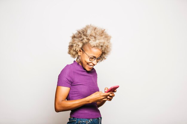 Portrait de jeune femme souriante à l'aide d'un téléphone intelligent en se tenant debout sur fond blanc