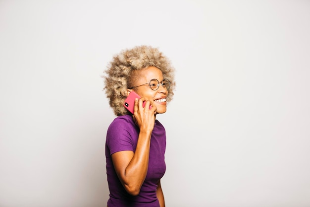 Portrait de jeune femme souriante à l'aide d'un téléphone intelligent en se tenant debout sur fond blanc