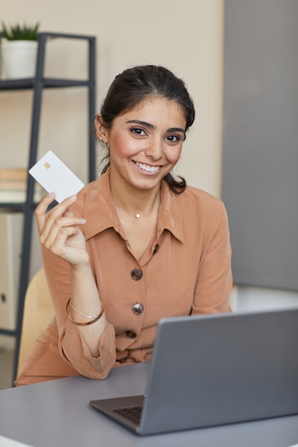 Portrait de jeune femme souriante à l'avant alors qu'il était assis à la table avec ordinateur portable et acheter des achats en ligne avec carte de crédit