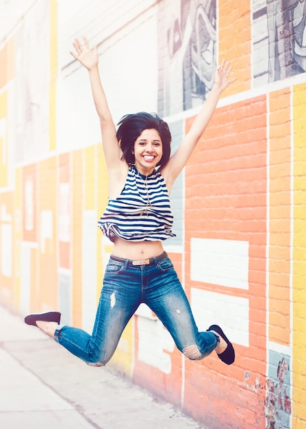 Photo portrait d'une jeune femme souriante avec les bras levés sautant contre le mur