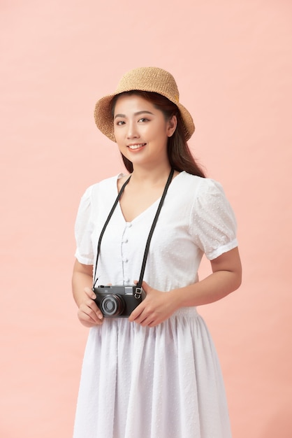 Portrait d'une jeune femme souriante en chapeau d'été debout avec appareil photo isolé sur rose