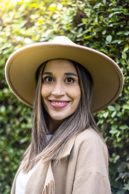 Portrait d'une jeune femme souriante dans un chapeau avec des feuilles vertes en arrière-plan à l'extérieur