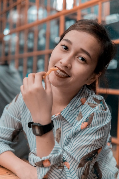 Portrait d'une jeune femme souriante mangeant des frites