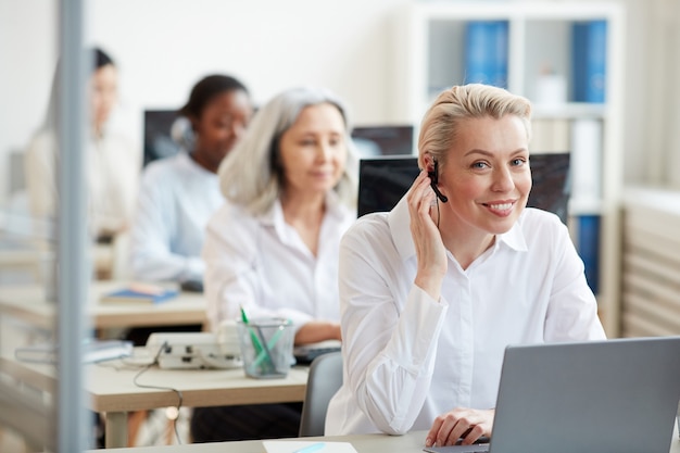 Portrait de jeune femme souriante portant un casque et à la recherche tout en travaillant comme opérateur de centre d'appels