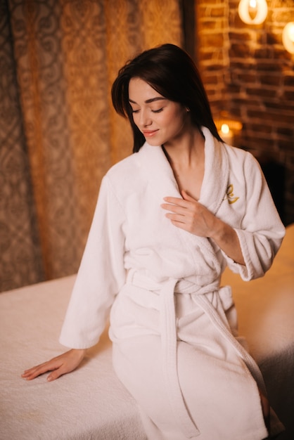 Portrait de jeune femme souriante en robe blanche assise sur une table de massage