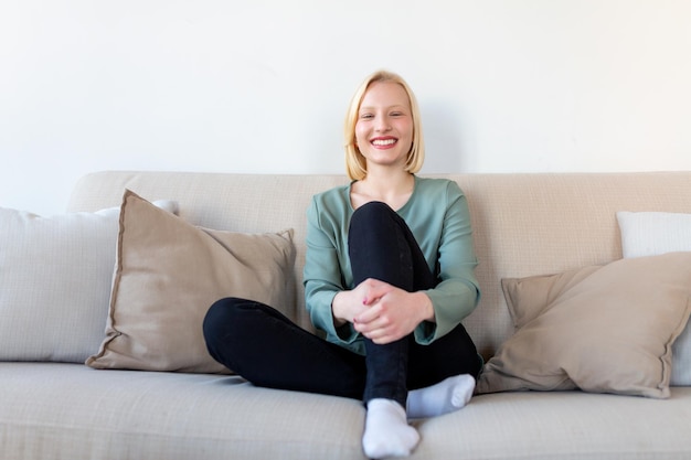 Portrait d'une jeune femme souriante se reposant seule sur son canapé du salon à la maison l'après-midi