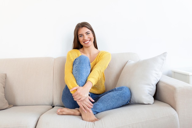 Portrait d'une jeune femme souriante se reposant seule sur son canapé du salon à la maison l'après-midi