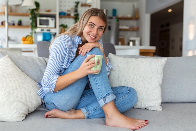 Portrait d'une jeune femme souriante se reposant seule sur son canapé du salon à la maison l'après-midi