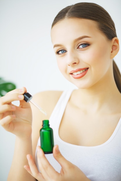 Portrait d'une jeune femme souriante tenant une bouteille verte avec des cosmétiques