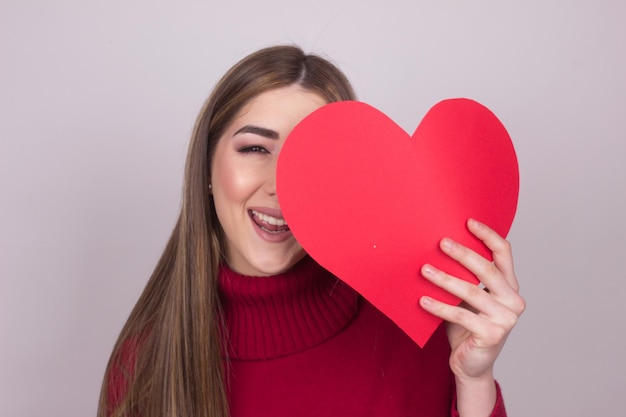 Portrait d'une jeune femme souriante tenant une forme de cœur sur un fond coloré