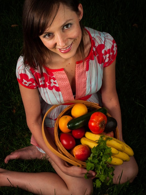 Portrait d'une jeune femme souriante tenant des légumes dans le panier.