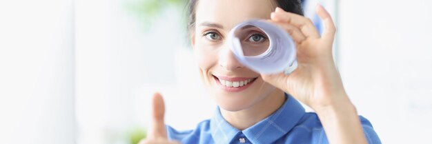 Portrait d'une jeune femme souriante tient les pouces vers le haut et regarde dans le tuyau en papier. Recherche de nouveau concept d'idées