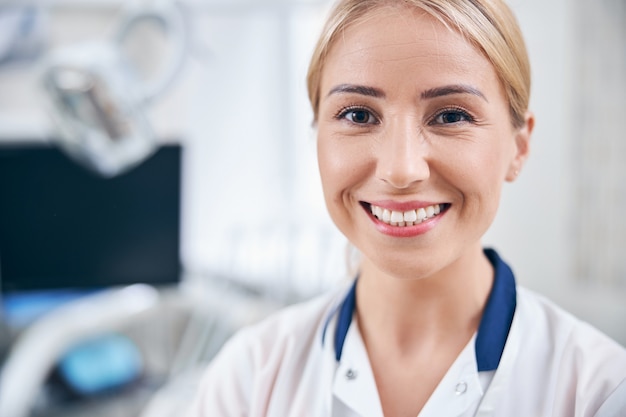 Portrait d'une jeune femme souriante en uniforme médical debout près d'un équipement moderne au bureau de la clinique