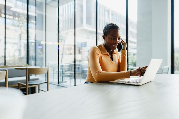 Portrait d'une jeune femme souriante utilisant un ordinateur portable et parlant sur un téléphone portable dans un café