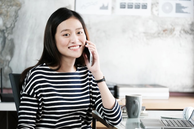 Portrait d'une jeune femme souriante utilisant un téléphone portable au bureau