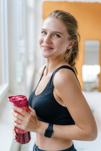 Portrait d'une jeune femme souriante en vêtements de sport buvant un smoothie