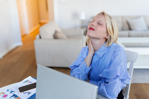 Portrait d'une jeune femme stressée assise au bureau à domicile devant un ordinateur portable touchant le cou douloureux avec une expression douloureuse souffrant de douleurs au cou après avoir travaillé sur un ordinateur portable