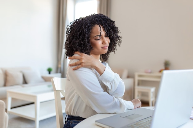 Portrait d'une jeune femme stressée assise au bureau à domicile devant un ordinateur portable touchant le dos douloureux avec une expression douloureuse souffrant de maux de dos après avoir travaillé sur un ordinateur