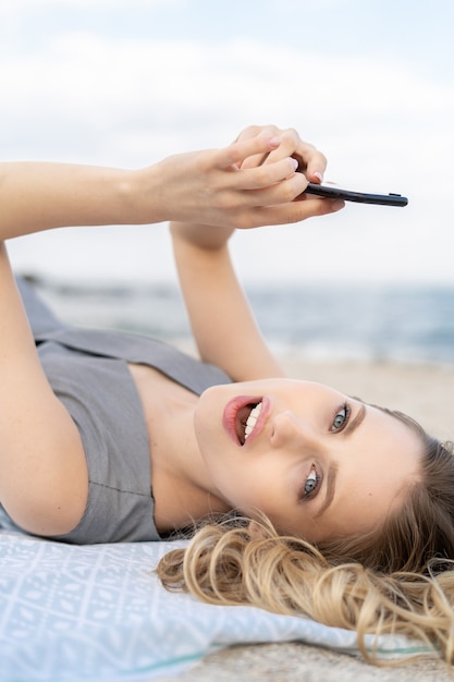 Portrait d'une jeune femme surprise tenant un téléphone portable et se trouve sur une plage