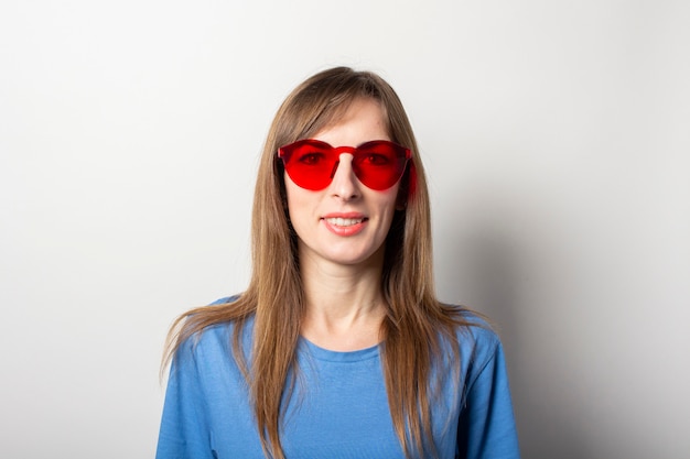 Portrait d'une jeune femme sympathique en t-shirt bleu décontracté et lunettes rouges souriant à la lumière isolée. Visage émotionnel