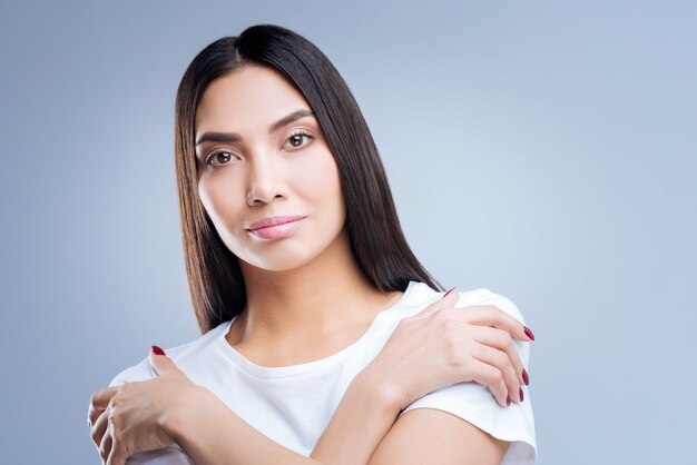 Portrait d'une jeune femme en t-shirt blanc posant contre un mur gris