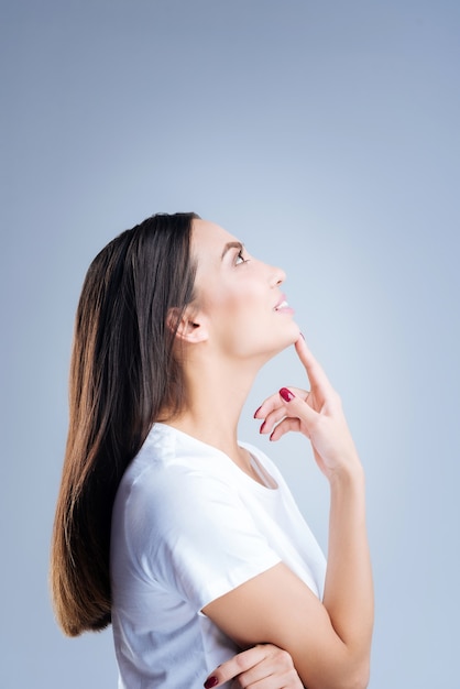 Portrait d'une jeune femme en t-shirt blanc posant contre un mur gris