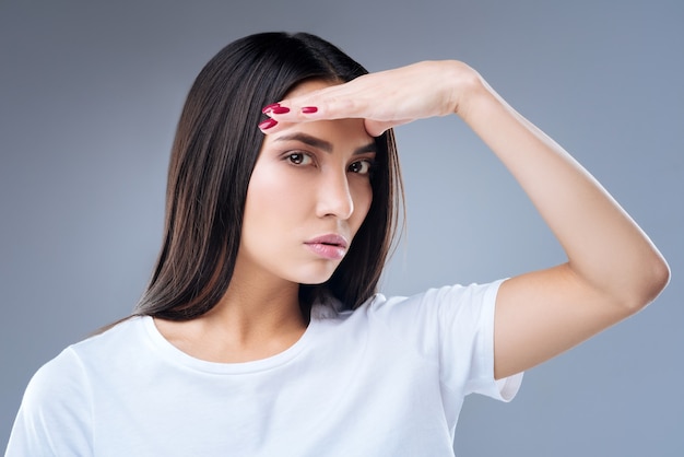 Portrait d'une jeune femme en t-shirt blanc posant contre un mur gris