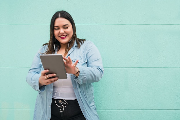 Portrait de jeune femme de taille plus écouter de la musique avec des écouteurs et une tablette numérique à l'extérieur.