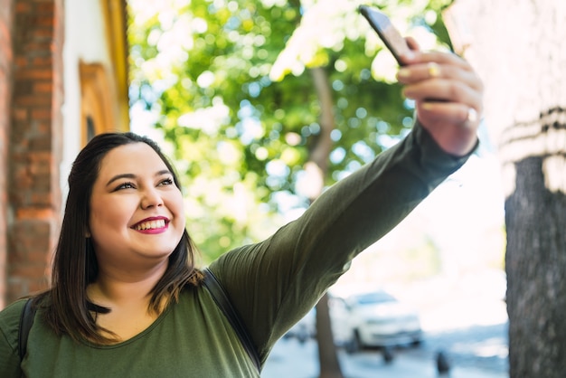 Photo portrait de jeune femme de taille plus prenant des selfies avec son téléphone mophile à l'extérieur dans la rue. concept urbain.