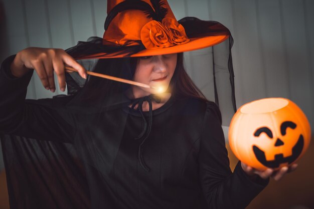 Photo portrait d'une jeune femme tenant une citrouille illuminée et une baguette magique contre le mur