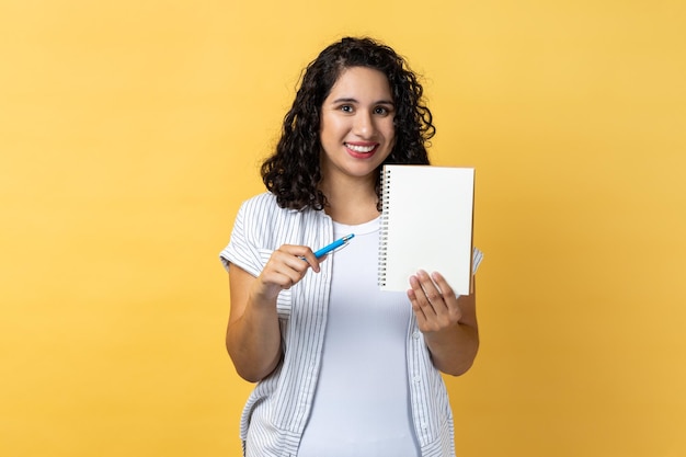 Photo portrait d'une jeune femme tenant un livre alors qu'elle se tient contre un fond jaune