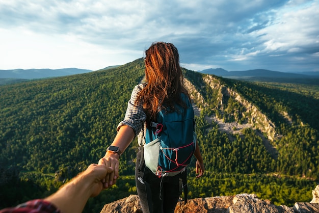 Portrait d'une jeune femme tenant la main de son petit ami en marchant le long d'une chaîne de montagnes. Le couple profite d'une randonnée dans la nature. Suivez-moi. Une fille tient la main de son petit ami dans les montagnes