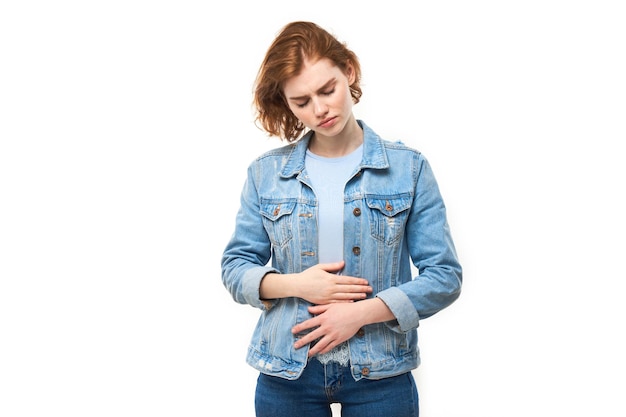 Portrait de jeune femme tenant les mains sur le ventre souffrant de douleurs menstruelles et d'inconfort intestinal isolé sur fond blanc