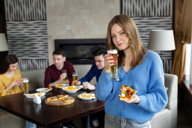 Portrait d'une jeune femme tenant une pizza et de la bière dans un pub