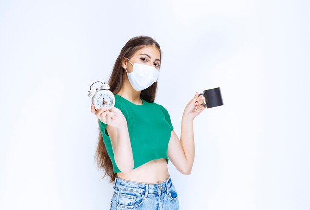 Portrait de jeune femme tenant une tasse de thé et une horloge sur fond blanc.