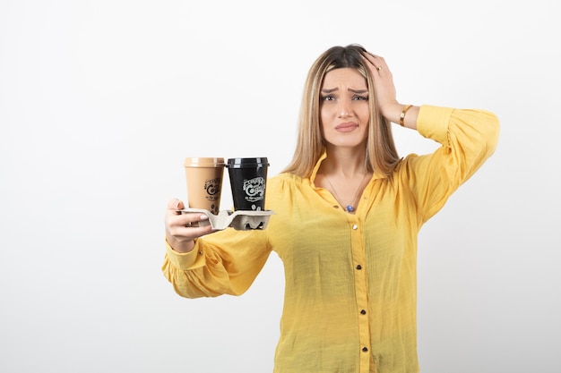 Portrait de jeune femme tenant des tasses de café et debout sur blanc.