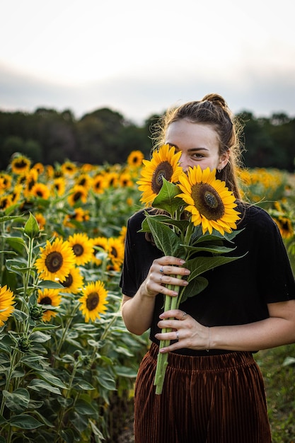Portrait d'une jeune femme tenant des tournesols alors qu'elle se tient à la ferme
